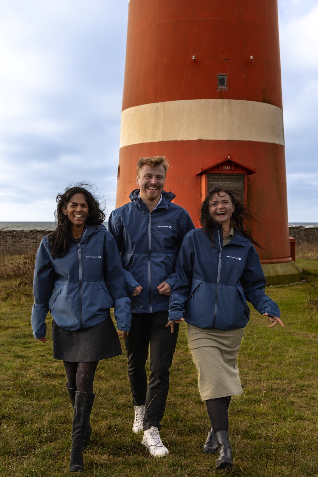 Tre glada människor framför en fyr